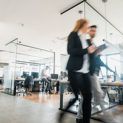 Business colleagues walking and talking near rows of desks in a bright office