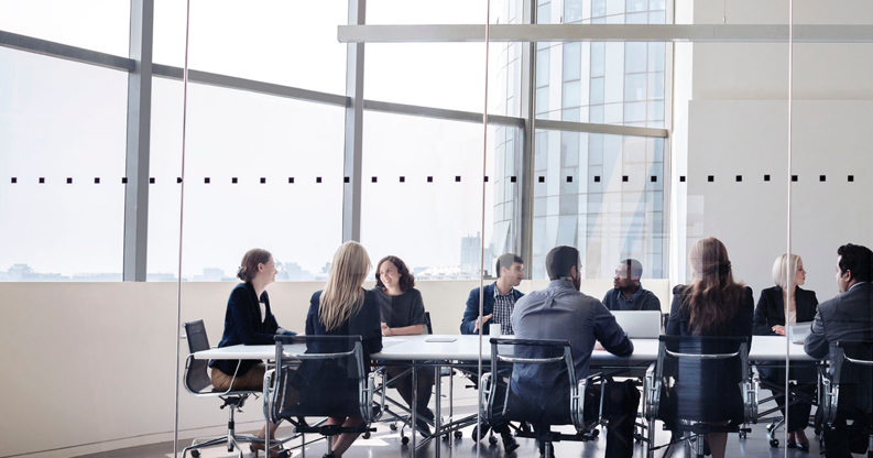 Colleagues at business meeting sitting at a long table in conference room