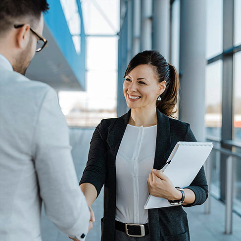 Business people smiling and shaking hands near office building windows