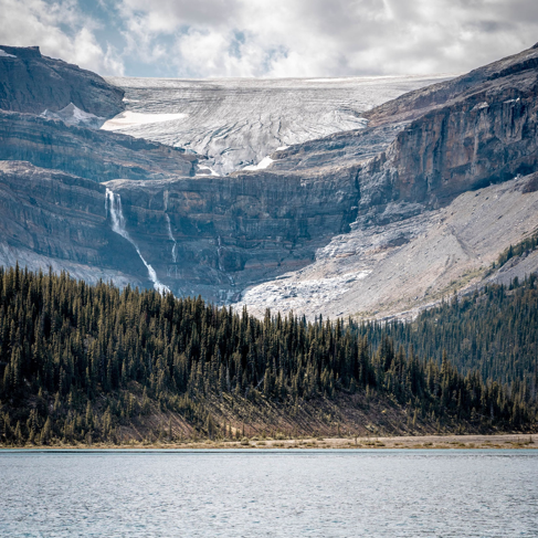 Snow-capped mountain covered in fog near body of water and trees