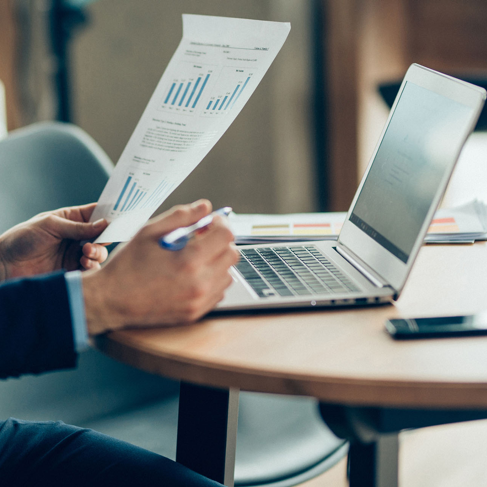 Hands of businessman reviewing graphs on paper near a laptop