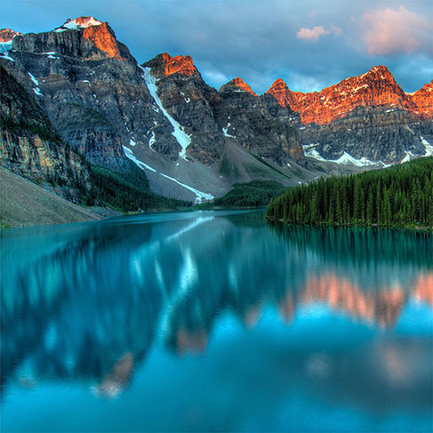 Coucher de soleil illuminant les montagnes près du lac réfléchissant et forêt de pins verts