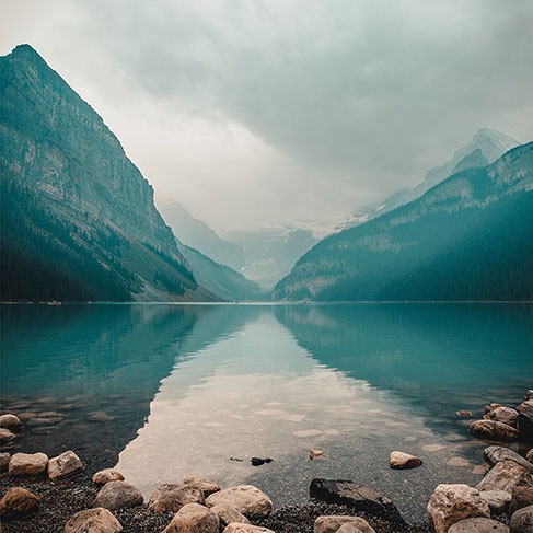 
Rive du lac rocheux avec des montagnes en arrière-plan pendant une journée nuageuse